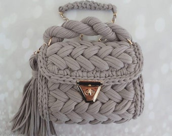 May include: A gray crocheted handbag with a braided handle and a gold clasp. The bag has a tassel on the side.