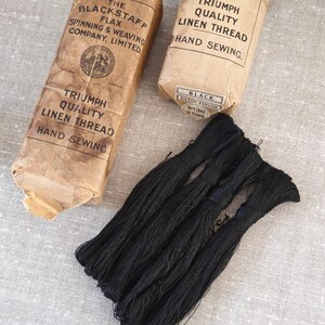 May include: Two rectangular paper-wrapped bundles of black linen thread and a loose cluster of black thread. The packaging is labelled The Blackstaff Flax Spinning & Weaving Company Limited, Triumph Quality Linen Thread, Hand Sewing, Black, Satin Finish, No 30, 2 Cord.