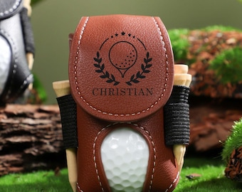 May include: Brown leather golf ball holder with a golf ball, tee, and a personalized name "CHRISTIAN" engraved on the front.