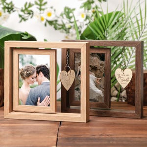 May include: Two wooden picture frames with a heart-shaped wooden charm hanging from each. The frames are both light brown and have a double-sided design. The charms are engraved with the text "Mr. & Mrs. Hill" and "Mr. & Mrs. Smith".