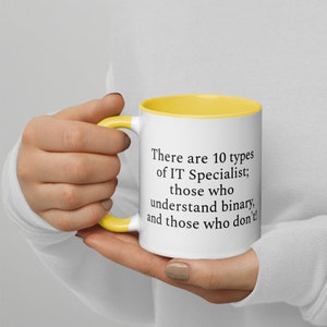 May include: A white coffee mug with a yellow rim and handle. The mug has black text that reads "There are 10 types of IT Specialist; those who understand binary, and those who don't!"