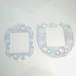 May include: Two light blue light switch covers with a wintery Hello Kitty design. The covers feature snowflakes, hearts, and Hello Kitty characters wearing winter hats and scarves.