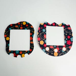 Pode incluir: Duas tampas de interruptor de luz pretas com um padrão Hello Kitty. O padrão apresenta Hello Kitty, flores e outros desenhos em vermelho, amarelo, azul e branco sobre um fundo preto. Uma tampa tem uma forma retangular arredondada, e a outra tem uma forma oval arredondada.