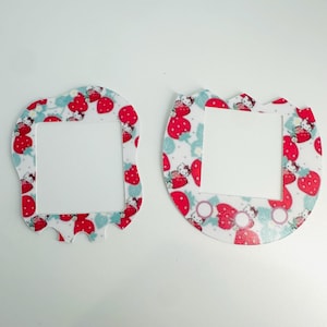 Pode incluir: Duas molduras decorativas com um centro branco e um padrão de morangos e personagens. As molduras têm um fundo branco com morangos vermelhos, folhas azuis e uma personagem de desenho animado. Uma moldura tem uma forma única.