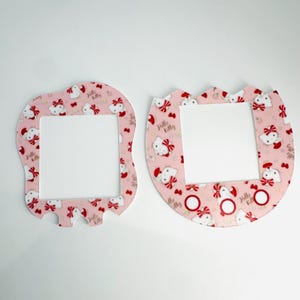 Pode incluir: Duas folhas de adesivos rosa com tema Hello Kitty para um console de jogos portátil. As folhas apresentam um padrão repetitivo de Hello Kitty usando um chapéu de Papai Noel vermelho e um laço vermelho. As folhas são projetadas para se ajustar à tela e aos botões do console.