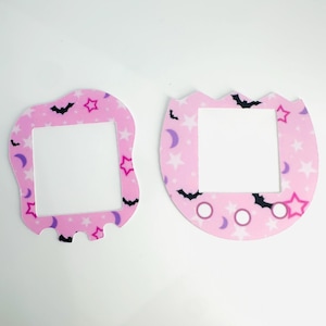 Può includere: Due placche per interruttori della luce rosa con un design fantasioso che presenta pipistrelli, stelle e mezze lune. Le placche sono realizzate in un materiale strutturato e hanno un bordo bianco attorno all'apertura dell'interruttore.