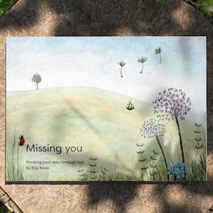 May include: A book cover with a watercolor illustration of a green hill, a small tree, a bee, and dandelions. The title of the book is "Missing you" and the subtitle is "Working your way through loss" by Fay Bloor.