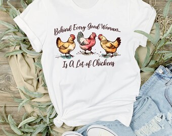 May include: White t-shirt with a humorous saying about chickens. The text reads "Behind Every Good Woman... Is A Lot of Chickens". Three cartoon chickens are depicted below the text.