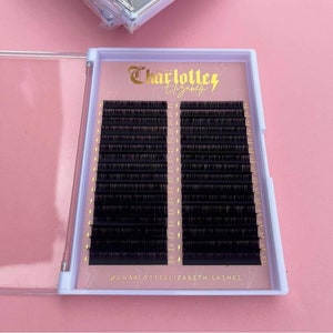 Könnte beinhalten: Geöffnete weiße Hülle mit schwarzen Wimpernverlängerungen. Die Hülle hat ein rosa Innenfutter mit goldenem Text, der "Charlotte Elizabeth" und den Instagram-Handle @charlotteelizabeth.lashes zeigt. Die Wimpern sind in Reihen mit Längenmarkierungen angeordnet.