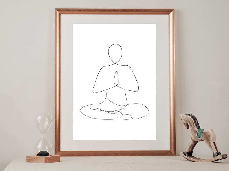 Puede incluir: Una impresi&oacute;n art&iacute;stica minimalista enmarcada. La obra representa a una persona en una postura de yoga sentada con las manos en oraci&oacute;n. La impresi&oacute;n est&aacute; en un marco dorado. Un caballo balanc&iacute;n de madera y un reloj de arena est&aacute;n en el fondo.