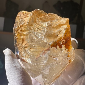 May include: A large, clear, faceted quartz crystal with a golden hue. The crystal has a rough, natural texture and is partially translucent.