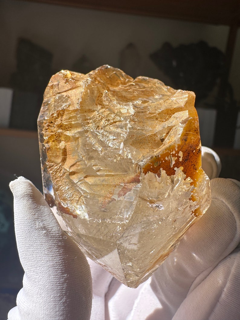 May include: A large, clear, faceted quartz crystal with a golden hue. The crystal has a rough, natural texture and is partially translucent.