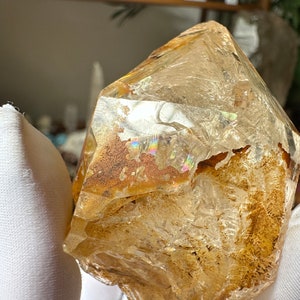 May include: A large, clear quartz crystal with a golden hue and iridescent inclusions. The crystal has a rough, natural shape and is a beautiful example of raw quartz.