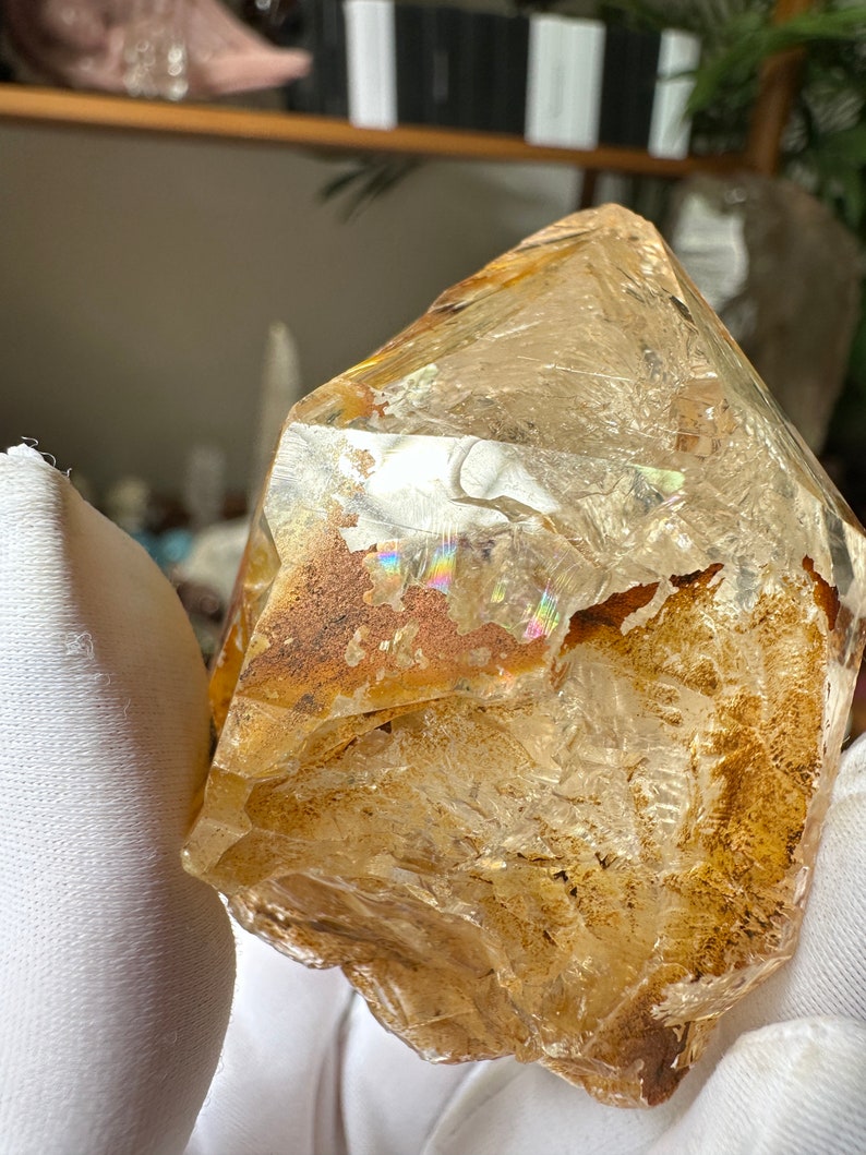 May include: A large, clear quartz crystal with a golden hue and iridescent inclusions. The crystal has a rough, natural shape and is a beautiful example of raw quartz.