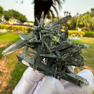 May include: A cluster of green and clear quartz crystals with a sharp, pointed shape. The crystals are arranged in a random pattern, creating a unique and interesting display.