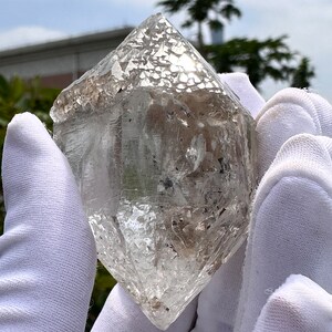 Puede incluir: Un gran cristal transparente facetado con un aspecto ligeramente nublado. El cristal se sostiene con guantes blancos.