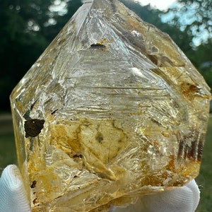 May include: A large, clear quartz crystal with a golden hue and inclusions. The crystal is faceted and has a natural, rough texture.
