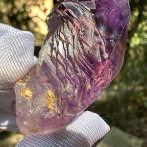 Może przedstawiać: Duży, fioletowy kryształ ametystu o spiczastym zakończeniu i przejrzystej, szklistoj strukturze. Kryształ ma naturalną, szorstką powierzchnię i wykazuje skomplikowane wewnętrzne prążki.