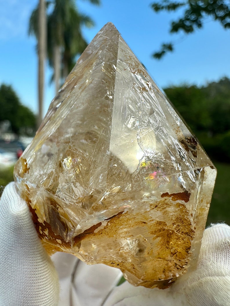 May include: A large, clear quartz crystal with a golden brown hue. The crystal has a pointed tip and a rough, natural surface. It is a beautiful example of a natural crystal.