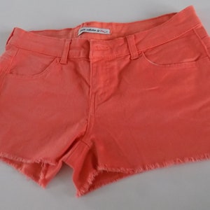 Puede incluir: Shorts vaqueros de color coral con dobladillo deshilachado. Los shorts tienen un diseño clásico de cinco bolsillos, trabillas para el cinturón y cierre de botón. Los shorts están hechos de un material de mezclilla suave. La etiqueta dice "petite collection by Vian".