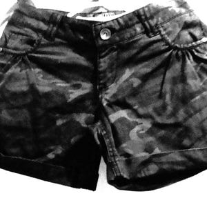 Könnte beinhalten: Schwarze und graue Shorts mit Tarnmuster und umgeschlagenem Saum.
