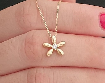 May include: A gold chain necklace with a small flower pendant featuring a single clear stone in the center.