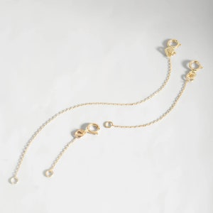 May include: Three gold chain extenders with lobster claw clasps. The extenders are different lengths.