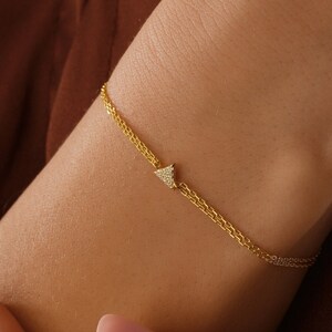 May include: A gold chain bracelet with a small triangle-shaped charm set with tiny clear stones.
