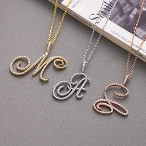 Könnte beinhalten: Drei Halsketten aus Gold, Silber und Roségold mit diamantbesetzten Initialanhängern. Die Anhänger sind in Form der Buchstaben M, A und E.