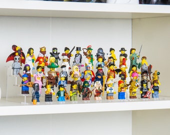 May include: A collection of Lego minifigures displayed on a white shelf. The figures are diverse, with various outfits and accessories. A white Lego shoe is on the left. Other Lego figures are on the top shelf.