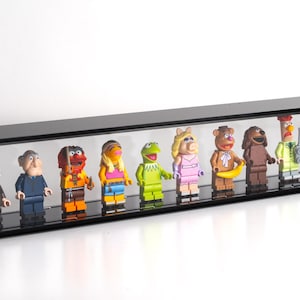 May include: A clear display case with a black top and base, showcasing a collection of Muppet character figurines. The figurines are colourful and detailed, including characters like Kermit the Frog and Miss Piggy.
