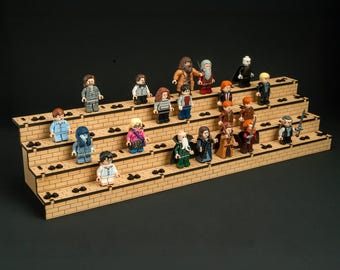May include: A tiered, light brown wooden display stand with a brick-patterned surface, featuring numerous small plastic character figurines arranged across four levels. The stand has black circular studs integrated into the wooden tiers.