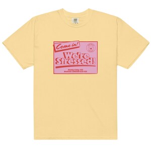 K&ouml;nnte beinhalten: Ein gelbes T-Shirt mit einer pinkfarbenen und roten Grafik, auf der "Come in! We're Stressed!" steht, darunter der Text "Monday-Friday: YES! Weekends: SOMEHOW ALSO YES!"