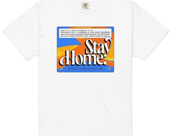 Puede incluir: Camiseta blanca con un gráfico azul, naranja y amarillo que dice "Stay Home". El gráfico es de estilo retro.