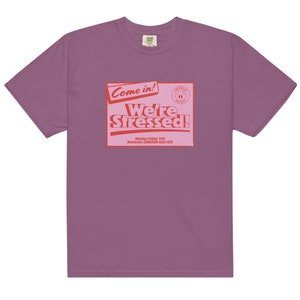 K&ouml;nnte beinhalten: Ein lila T-Shirt mit einer roten Grafik, auf der "Come in! We're Stressed!" steht, darunter der Text "Monday-Friday: YES! Weekends: SOMEHOW ALSO YES!"