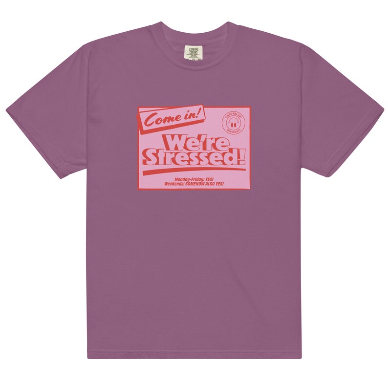 K&ouml;nnte beinhalten: Ein lila T-Shirt mit einer roten Grafik, auf der "Come in! We're Stressed!" steht, darunter der Text "Monday-Friday: YES! Weekends: SOMEHOW ALSO YES!"