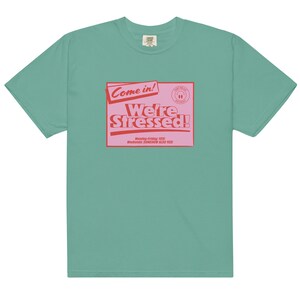 K&ouml;nnte beinhalten: Ein blaugr&uuml;nes T-Shirt mit einer pinkfarbenen und roten Grafik, auf der "Come in! We're Stressed!" steht, darunter der Text "Monday-Friday: YES! Weekends: SOMEHOW ALSO YES!"