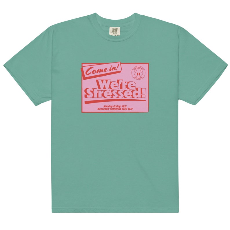 K&ouml;nnte beinhalten: Ein blaugr&uuml;nes T-Shirt mit einer pinkfarbenen und roten Grafik, auf der "Come in! We're Stressed!" steht, darunter der Text "Monday-Friday: YES! Weekends: SOMEHOW ALSO YES!"