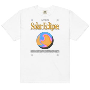 Op de afbeelding: Wit T-shirt met een grafische print van een draaiende, kleurrijke planeet met een zwarte halve maan. De tekst "I survived the Solar Eclipse" is in geel boven de planeet gedrukt. Het jaar 2004 is in kleine cirkels aan beide kanten van de tekst gedrukt.