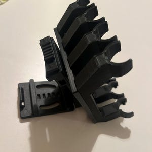 May include: Black plastic clip-on organizer with multiple slots. The organizer has a rectangular base and a series of curved arms designed to hold items. The item is designed to be clipped onto something.