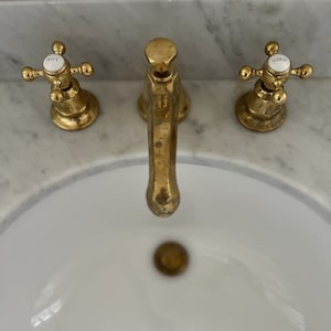 May include: A white porcelain sink with a gold faucet and two gold knobs labeled "HOT" and "COLD".