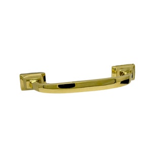 May include: A gold-colored cabinet pull with a curved handle and square end pieces. The hardware has a shiny, reflective surface and is designed for furniture. The pull is shown against a white background.