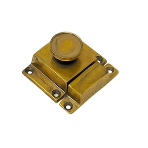 May include: A brass cabinet latch with a round knob. The latch has a square shape and is designed to be mounted on a cabinet door.