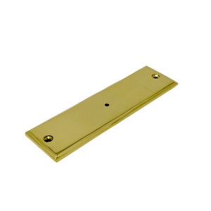 May include: A solid brass rectangular plate with rounded edges and two small holes. The plate is a light gold color.