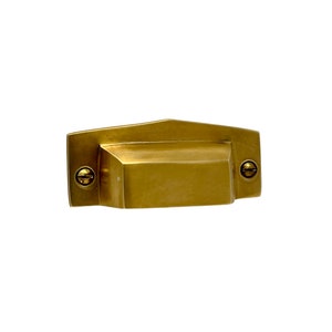 May include: A gold-toned metal cabinet pull with a rectangular shape and rounded edges. The pull has two small screws on either side.