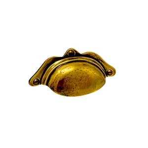 May include: A brass cabinet pull with a rounded, oval-shaped design. The pull has a slightly textured surface and is accented with small, round rivets.
