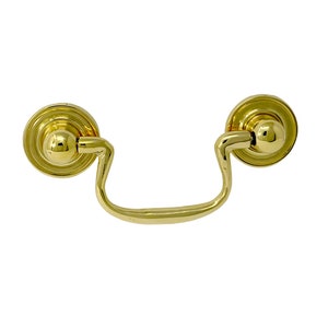 May include: A polished brass drawer pull with a bail handle. The pull features two circular backplates with a raised, rounded design. The handle is a curved, U-shaped bar. The hardware is designed for cabinets and drawers.