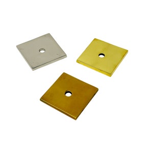 May include: Three square metal plates with a hole in the center. One plate is silver, one is gold, and one is a darker gold.