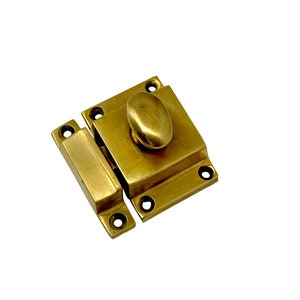 May include: A brass cabinet latch with a rounded knob. The latch has a square base and a rectangular arm.