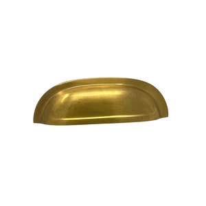 May include: A gold-toned cabinet pull with a curved, slightly rounded shape.